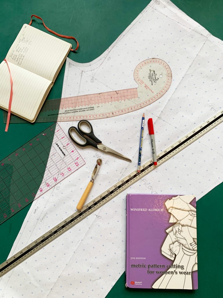 Flatlay of drafted leggings pattern piece, drafting tools, note book and pattern drafting book