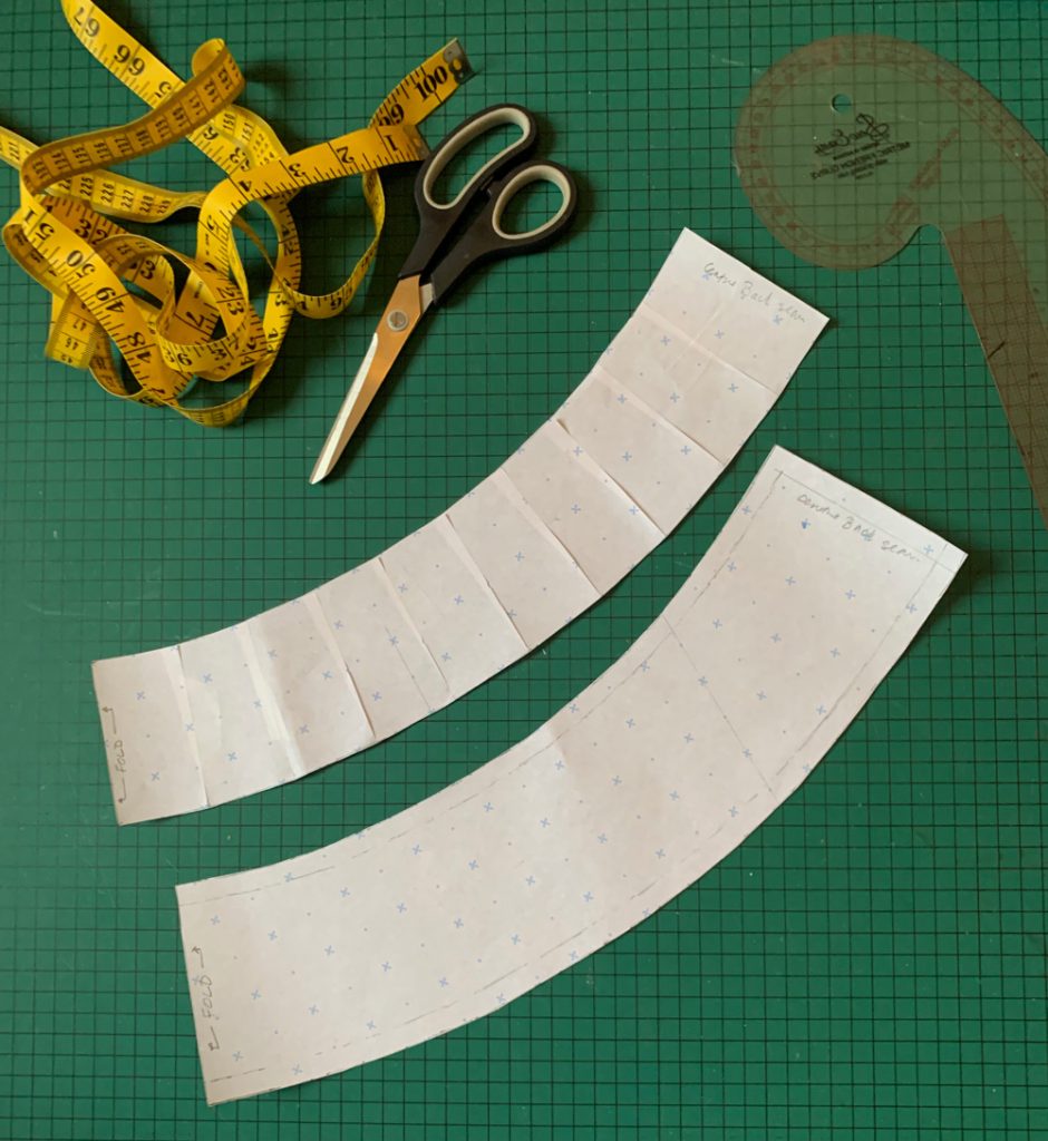 Flatlay of the drafted pattern pieces, one with and one without seam allowance, for the waistband. a tape measure and a pair of scissors are positioned next to the pattern pieces.